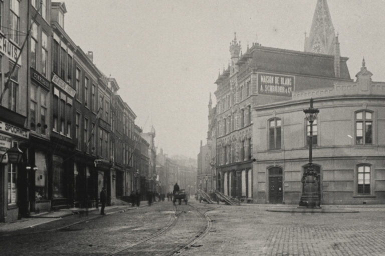 historische Aufnahme einer Straße in Den Haag, Straßenbahnschienen, große Laterne, Kirchturm mit Uhr, alte Häuser