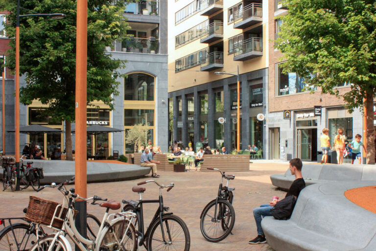 Räder, Person sitzt auf einer Bank, Neubauten in einem Stadtentwicklungsgebiet, Bäume, Laternen, Balkone, Geschäfte
