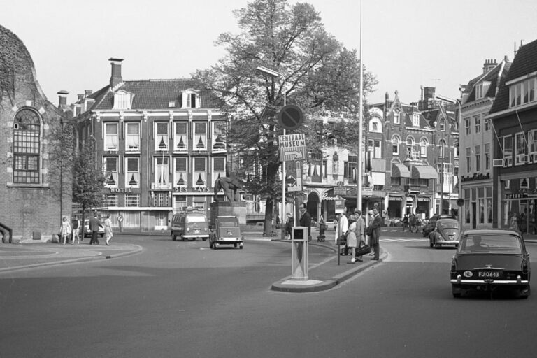 Platz in Utrecht, fahrende Autos, Baum, alte Häuser, Kirche, Leute warten an einer Bushaltestelle