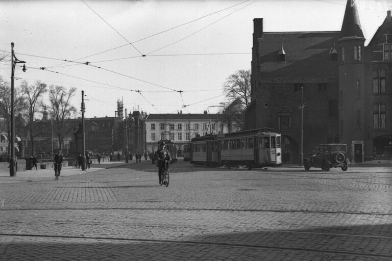 Mann fährt auf einem Fahrrad über einen Platz in Den Haag, Straßenbahn und Auto im Hintergrund