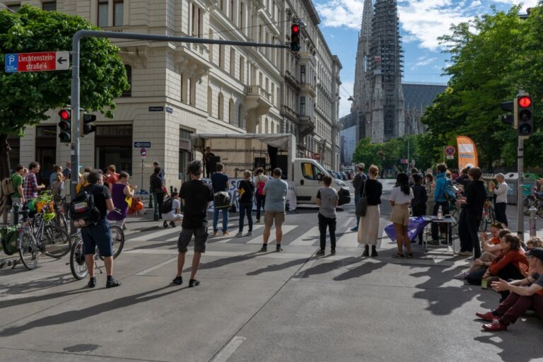 Leute stehen auf einer Straße vor einem Laster mit geöffneter Plane, Kundgebung