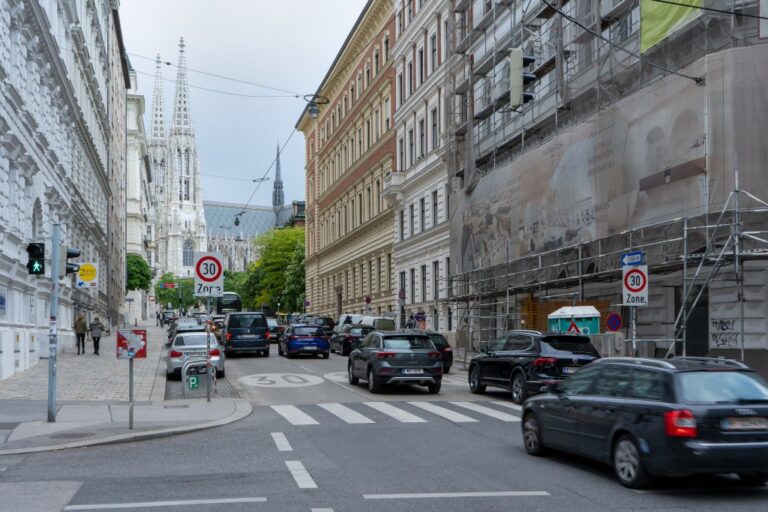 Autos fahren auf einer Straße in Richtung der Votivkirche, Gebäude rechts eingerüstet