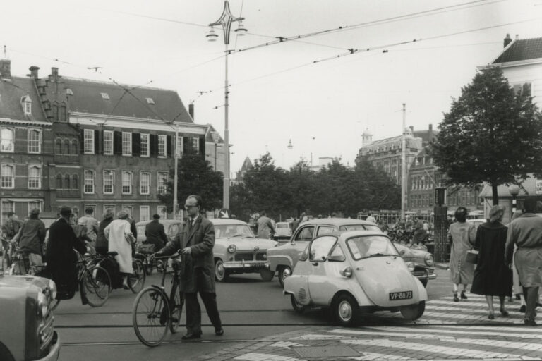 dichter Autoverkehr, Mann schiebt ein Fahrrad, Leute gehen über einen Zebrastreifen, Fahrradfahrer, Binnenhof