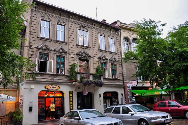 Gebäude in Ljubljana mit begrüntem Balkon, parkende Autos, Lokale, Bäume