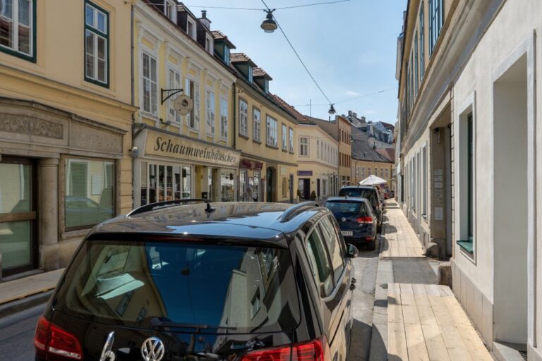 Gasse mit alten Häusern in Wien-Hietzing, parkende Autos, schmale Gehsteige mit Brettern, Hängeleuchten