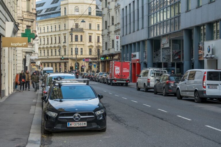 Straße in Wien mit parkenden Autos, Fußgänger, Geschäfte, Häuser