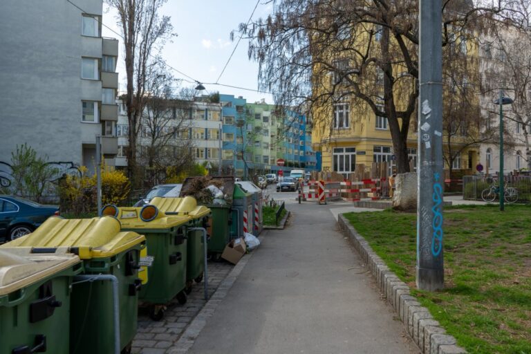 Gehsteig zwischen Müllcontainern und einem Park
