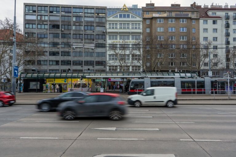 fahrende Autos auf einer Straße vor einer Häuserzeile in Wien