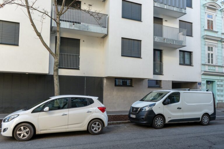 zwei Kfz parken vor einem Neubau in der Hugogasse, Baum, Balkone, Fenster