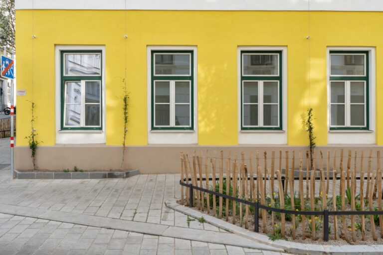 Erdgeschoßzone eines sanierten Altbaus mit Fassadenbegrünung, Grünfläche, Pflasterung
